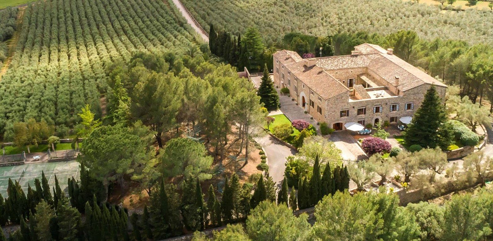 Aerial view of a large country estate on Mallorca with a historic stone main house, olive groves, gardens and tennis court