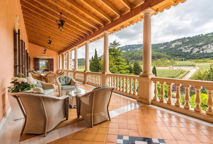 Covered loggia of a country estate with wicker furniture and views over vineyards to the Tramuntana mountains, Mallorca