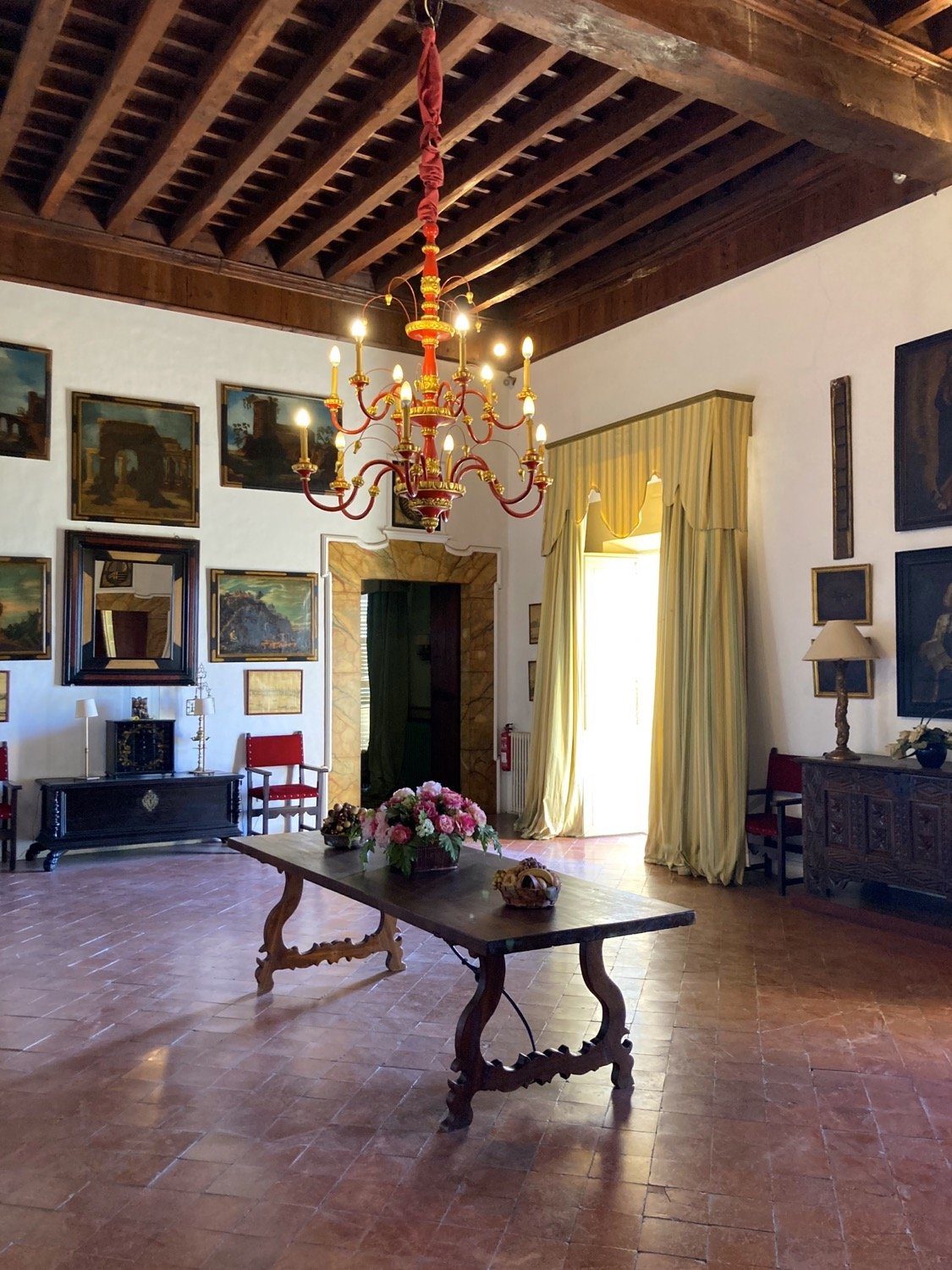 Grand salon of a historic Mallorcan manor house with timber-beamed ceiling, chandelier, old paintings and terracotta floor